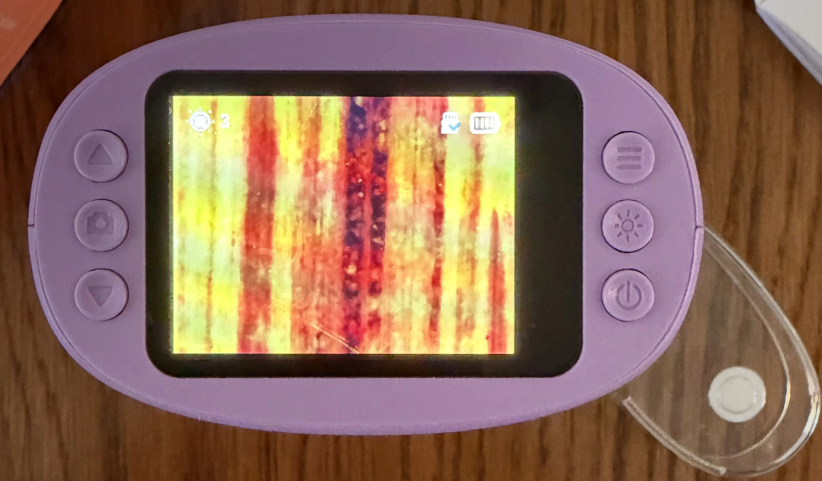 WonderQuest microscope powered on, showing a live magnified view of fabric with brightness, SD card and battery icons